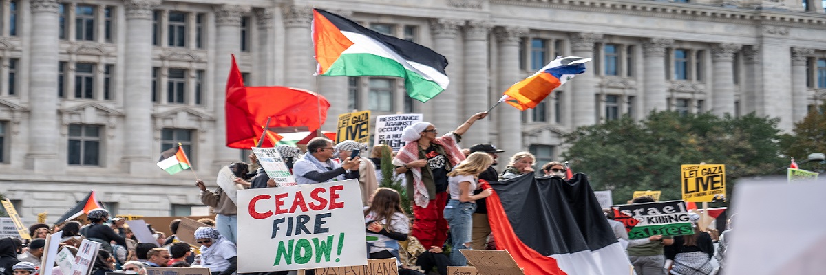 Protesters on the street holding Palestine flag and 'cease-fire now' banners